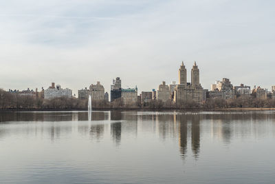 View of buildings by river against sky in city