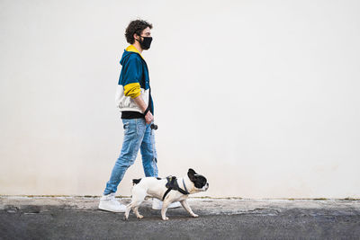Side view of hipster young man with safety mask with dog standing against wall