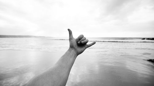 Close-up of hand showing shaka sign against beach