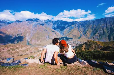 Rear view of couple sitting on mountain against sky