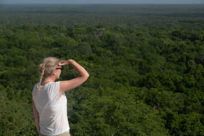 Young girl is looking over endless jungle at sunny day