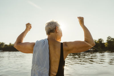 Rear view of senior woman flexing muscles on houseboat during vacation
