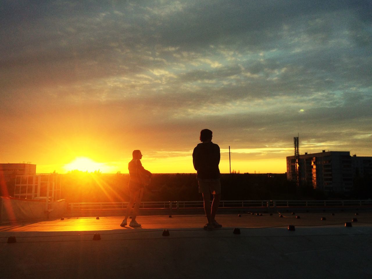 sunset, silhouette, sky, real people, leisure activity, skateboard, two people, men, cloud - sky, sun, full length, outdoors, sunlight, built structure, lifestyles, standing, architecture, building exterior, friendship, skateboard park, nature, city, day, people