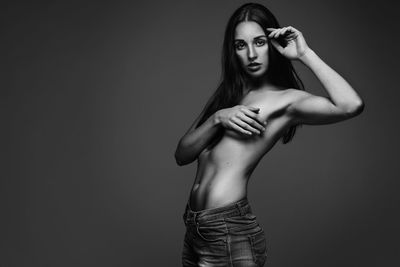 Portrait of shirtless woman covering breast while standing against gray background