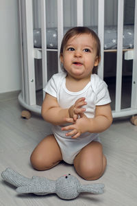 Child in white clothing one year sitting on the floor next to his round white bed