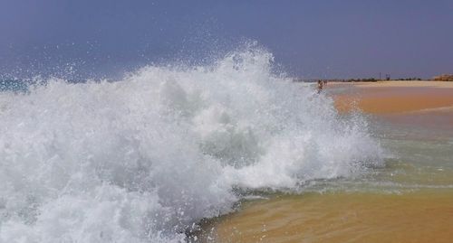 Waves splashing on shore against sky