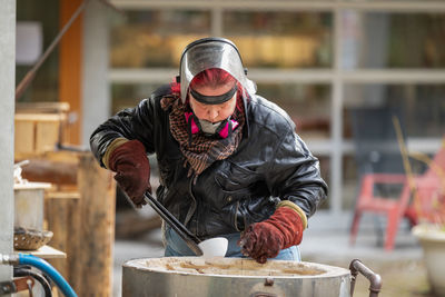 A red headed raku artist loading a ceramic bowl into updraft kiln, with tongs and protective gloves