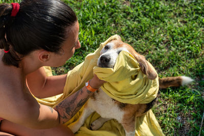 A tattooed girl in a bikini dries her old beagle dog with a yellow towel after the bath