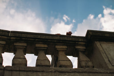 Low angle view of man climbing on railing against cloudy sky