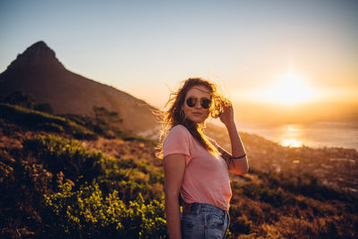 Woman standing on land against sky during sunset