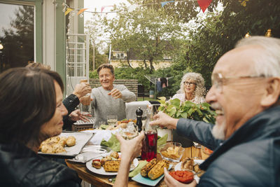 Happy senior male and female friends enjoying dinner party while sitting at dinning table in back yard