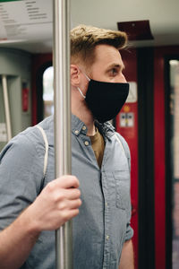 Man wearing mask holding metallic pole in train