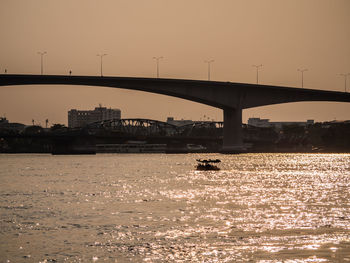 Silhouette bridge over river against sky during sunset