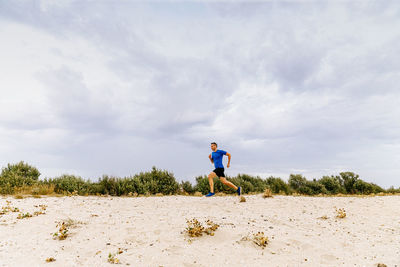 Male jogger running sandy beach in background evening sky