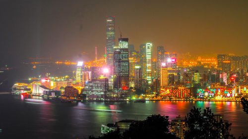 Illuminated buildings by river against sky at night