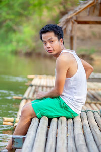 Young man sitting on wood against lake