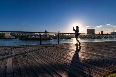 Rear view of woman standing on pier over sea against clear blue sky