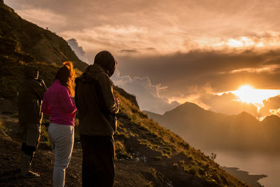 Rear view of man standing on mountain against sky during sunset