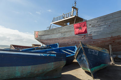 Low angle view of fishing boats moored at beach against sky