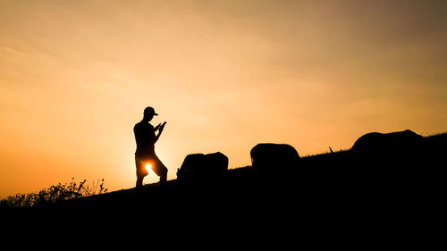 Low angle view of silhouette man using mobile phone on field against orange sky