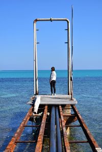 Rear view of woman standing on pier over sea against clear blue sky