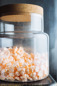 Sweet peach colored mini meringues in big glass jar placed on table next to window