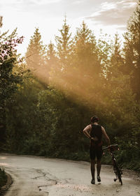 Rear view of man walking with bicycle on road amidst trees