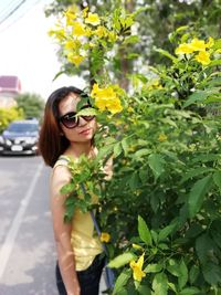 Portrait of young woman wearing sunglasses standing by flower plants
