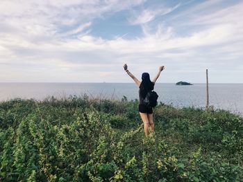 Full length of woman with arms raised in sea against sky