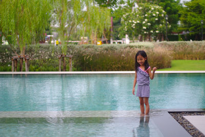 Portrait of a cute asian girl standing in the pool on a clear day. happily