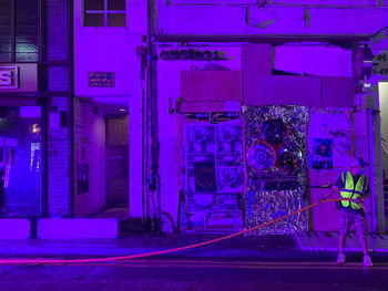 Illuminated street light on sidewalk against building at night