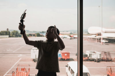 Cute boy taking selfie while standing against window in airport