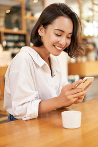 Young woman using mobile phone while sitting on table