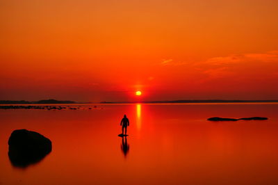 Silhouette woman walking on sea against sky during sunset