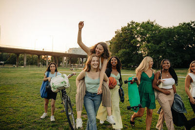 Happy teenage girl giving piggyback ride to female friend at park