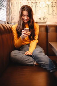 Happy teenage girl using smart phone while sitting in cafe