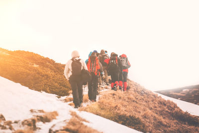 Hikers walking on mountain against clear sky during winter