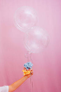 Close-up of hand holding transparent balloons on pink background.  colored scrunchis on the arm.