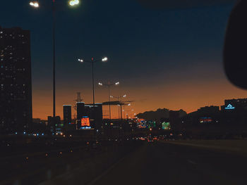 Illuminated street by buildings against sky at night