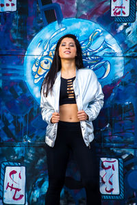 Portrait of young woman standing against graffiti