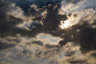 Low angle view of sunlight streaming through clouds