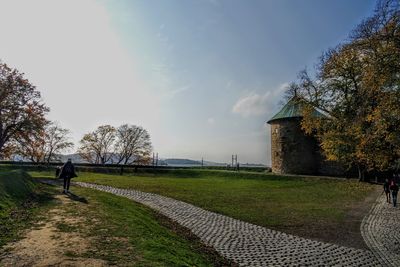 Rear view of man walking on footpath by field in fort against sky