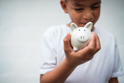 Midsection of boy holding piggy bank against white background