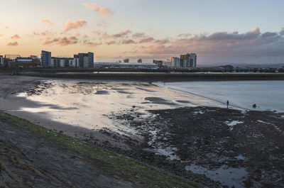 Buildings by sea against sky during sunset