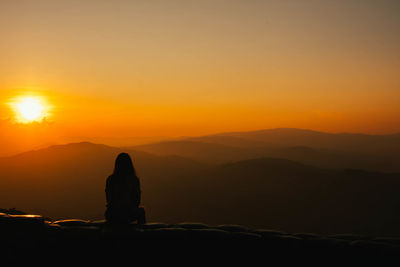 Silhouette man standing on mountain against orange sky