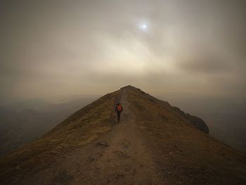 Rear view of man walking on mountain against sky