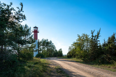 Lighthouse by trees against clear blue sky