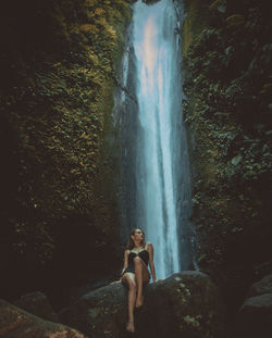 Woman sitting on rock against waterfall