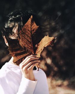 Close-up of woman covering face with dry maple leaf