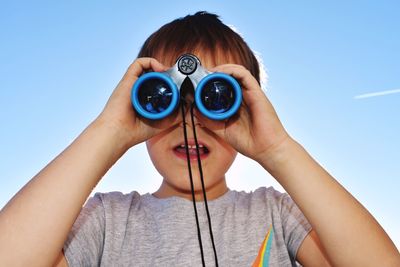 Portrait of woman holding camera against clear blue sky